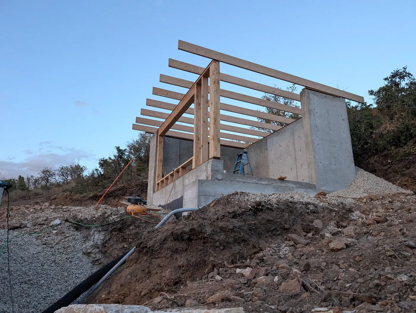 Site wall with timber roof framing — A concrete site wall carrying timber roof framing — combining retaining and gravity structure in one element